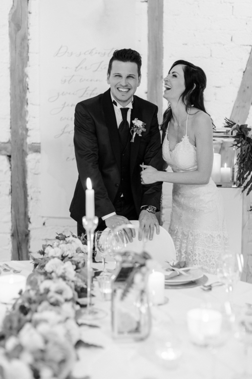 Lachendes Brautpaar am Hochzeitstisch in schwarz weiß im Landgut Halsberg in Hohenlohe